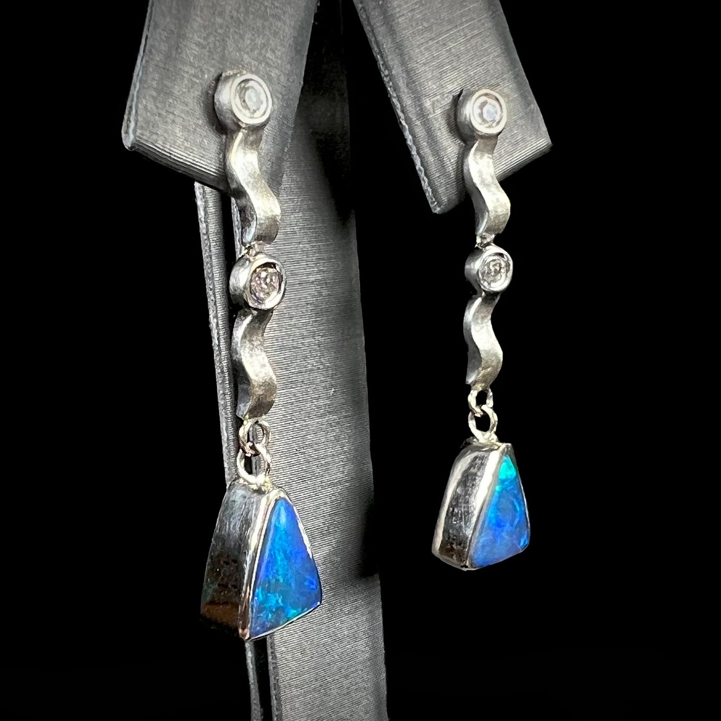 A pair of white gold earrings set with triangle cut natural black opals and round diamond accents.