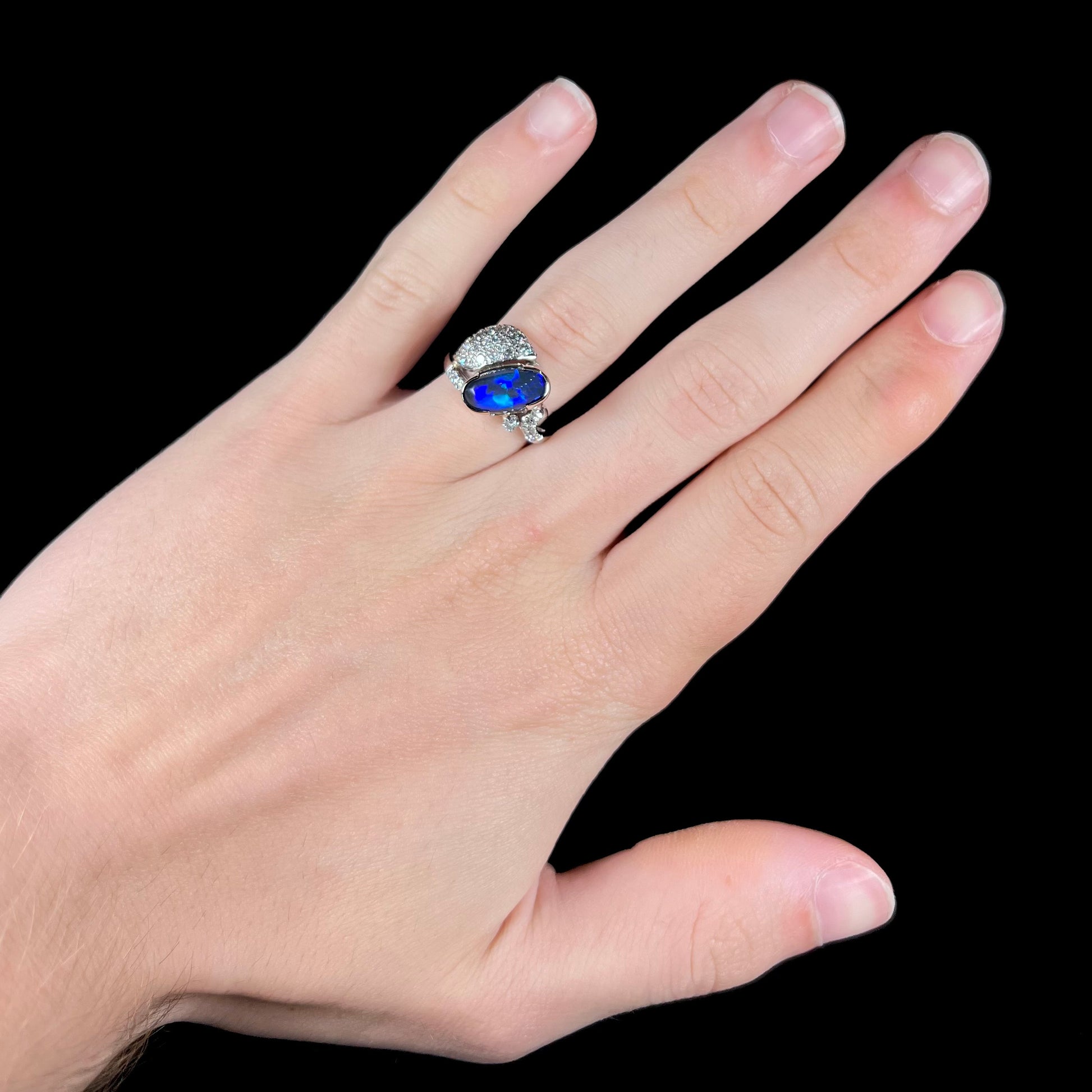 A platinum ring set with an oval cut black opal and round cut diamonds in a leaf design.