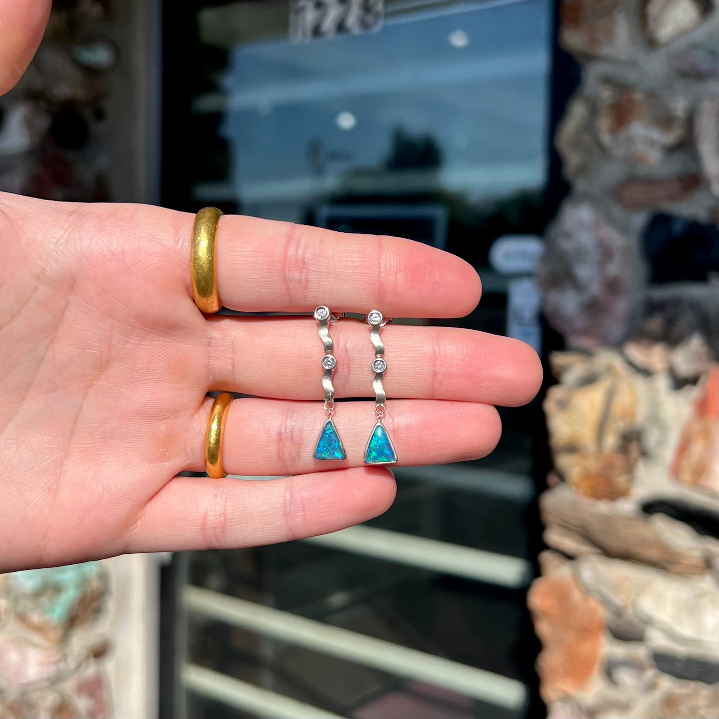 A pair of white gold earrings set with triangle cut natural black opals and round diamond accents.