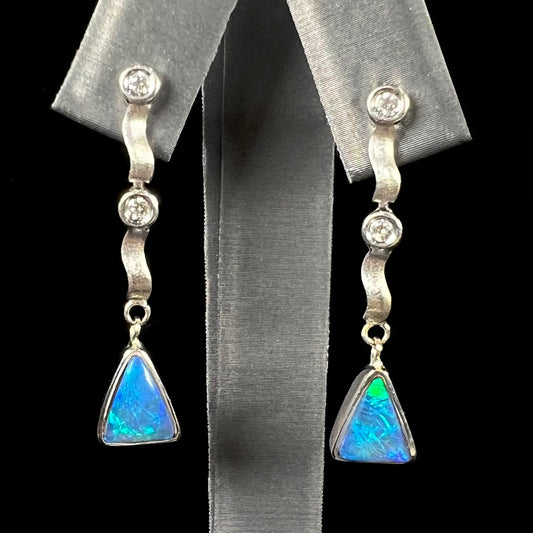 A pair of white gold earrings set with triangle cut natural black opals and round diamond accents.