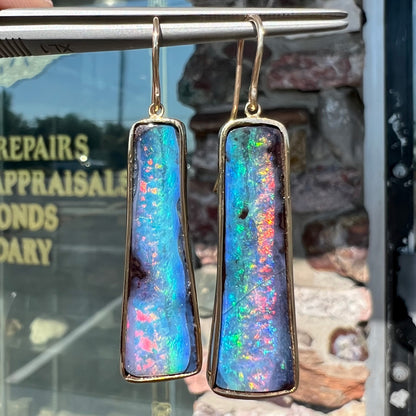 A pair of natural boulder opal dangle earrings set in yellow gold.  The opal displays a rainbow of colors and is from Bull Creek, Australia.