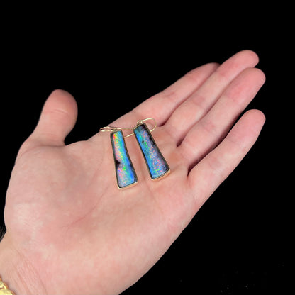 A pair of natural boulder opal dangle earrings set in yellow gold.  The opal displays a rainbow of colors and is from Bull Creek, Australia.