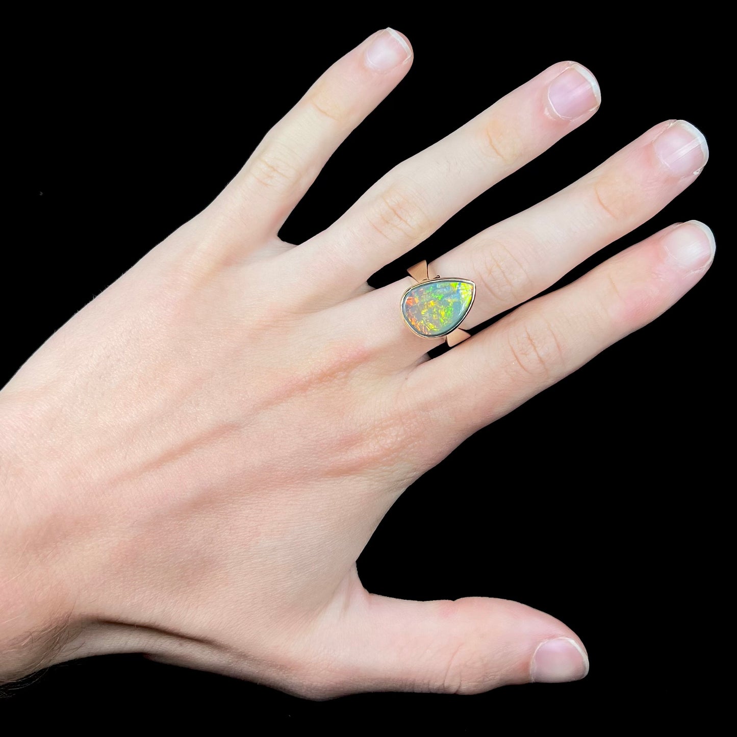 A large ladies' yellow gold solitaire ring set with a natural, pear shaped black crystal opal.  The opal has green and orange fire.