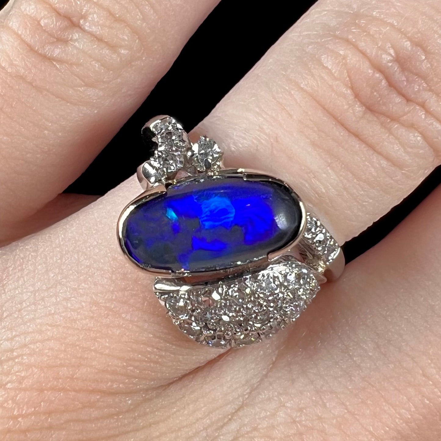 A platinum ring set with an oval cut black opal and round cut diamonds in a leaf design.