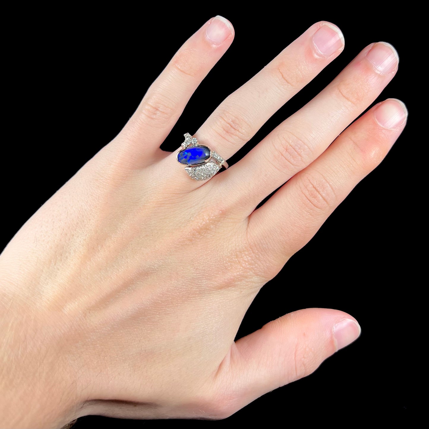 A platinum ring set with an oval cut black opal and round cut diamonds in a leaf design.