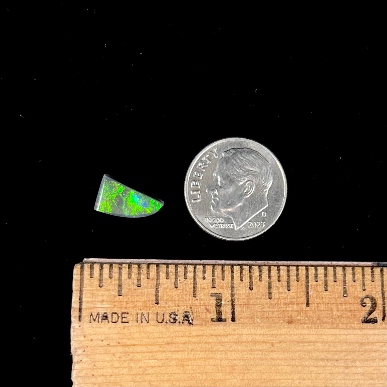 A loose, triangular shaped black opal stone from Lightning Ridge, Australia.  The opal has a bright green flash of color.