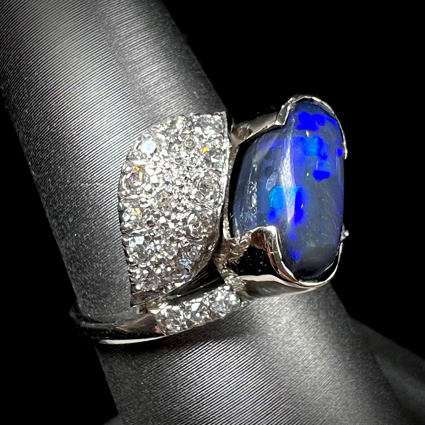 A platinum ring set with an oval cut black opal and round cut diamonds in a leaf design.