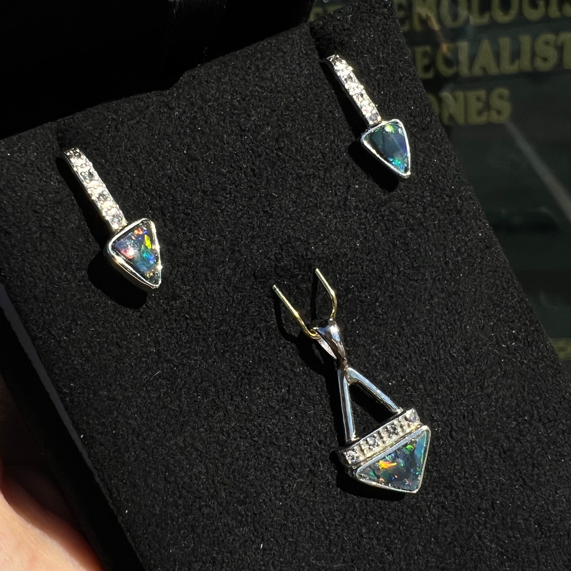 A white gold pendant and earrings set mounted with triangle cut natural black opals and diamonds.