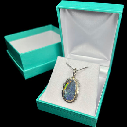 A two-tone silver and gold necklace set with a natural black boulder opal.  The necklace is in a blue box.