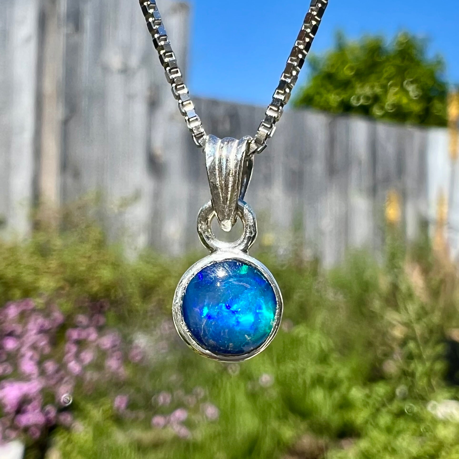 A sterling silver, round cabochon cut black opal solitaire necklace.  The opal has green and blue fire.