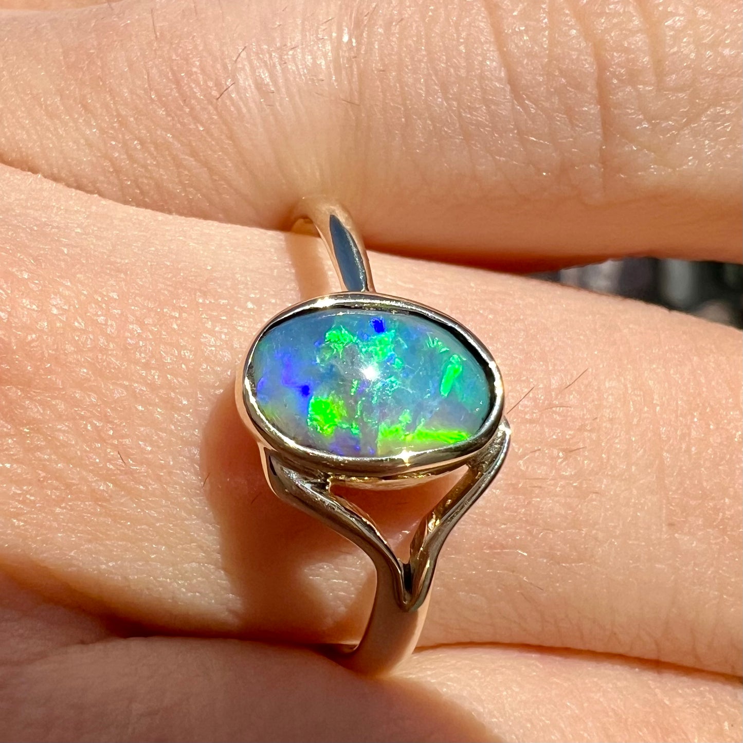 A ladies' oval cut black crystal opal solitaire ring handmade with a single split shank in yellow gold.