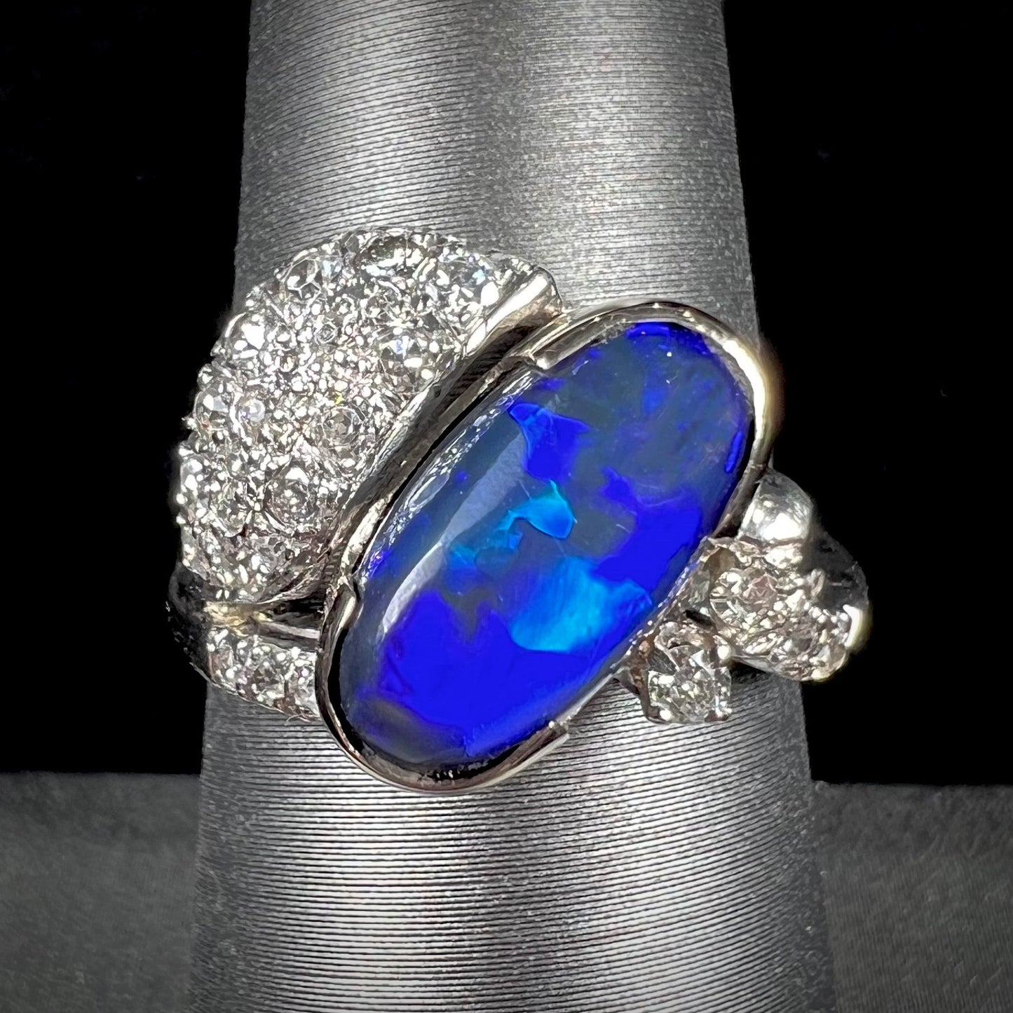 A platinum ring set with an oval cut black opal and round cut diamonds in a leaf design.