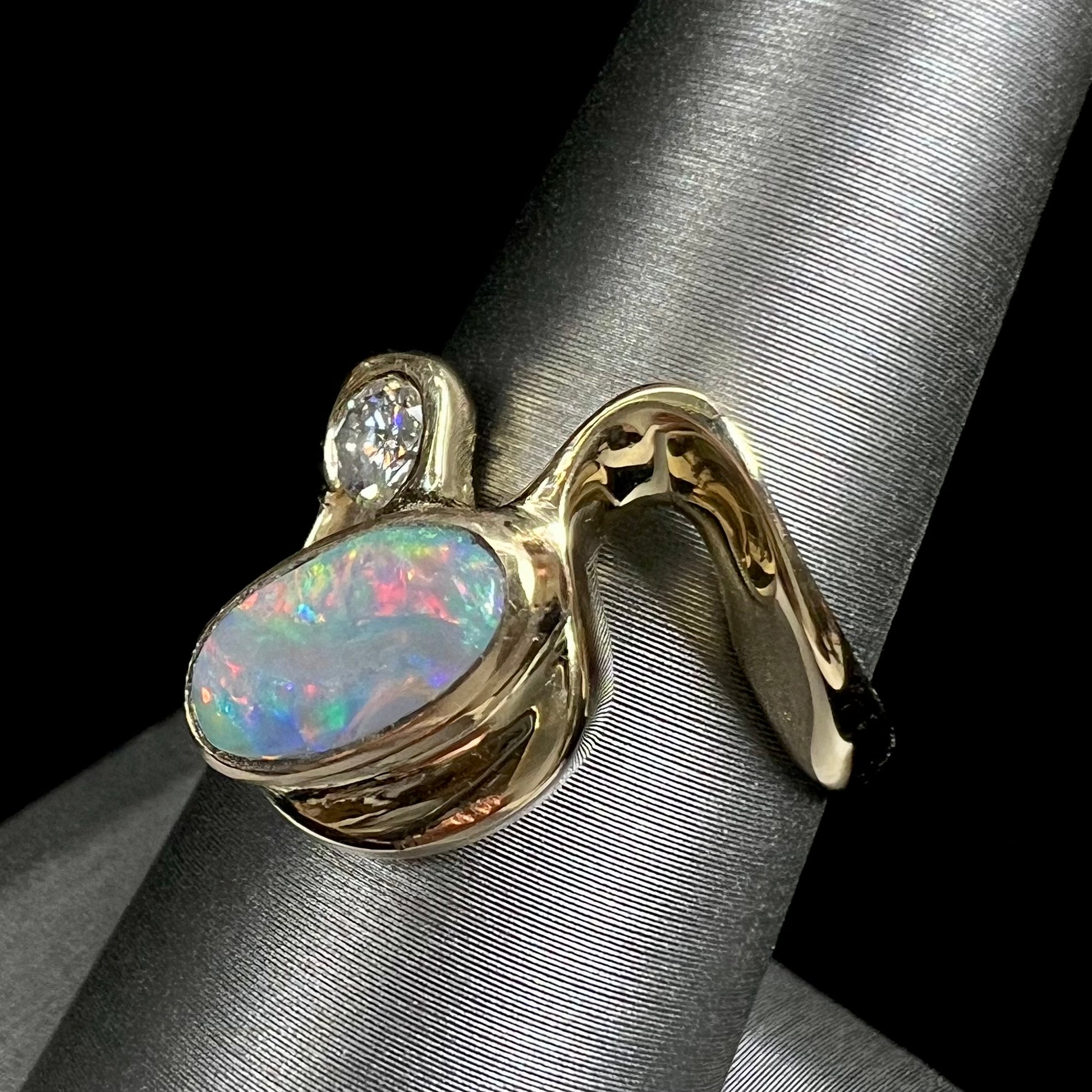 A ladies' yellow gold, bezel set ring mounted with a natural 1.15 carat black opal and round diamond.