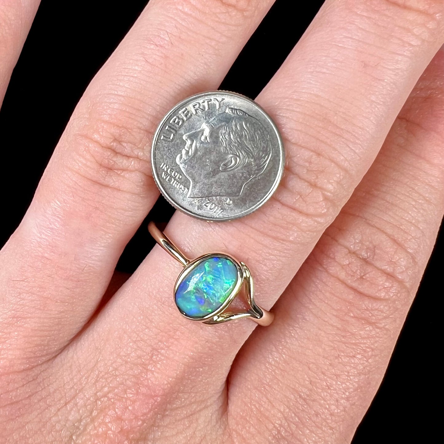 A ladies' oval cut black crystal opal solitaire ring handmade with a single split shank in yellow gold.