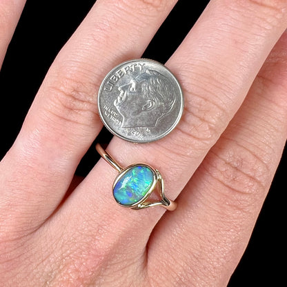 A ladies' oval cut black crystal opal solitaire ring handmade with a single split shank in yellow gold.