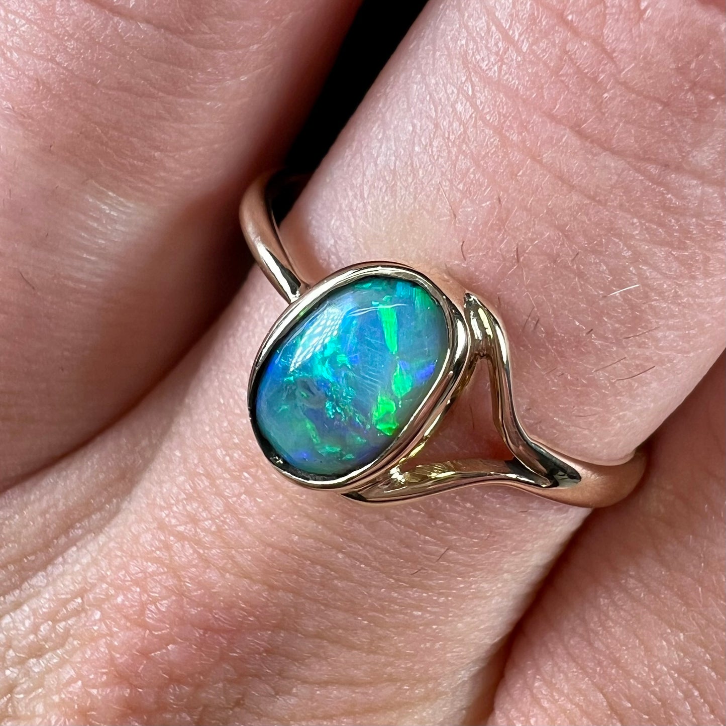 A ladies' oval cut black crystal opal solitaire ring handmade with a single split shank in yellow gold.