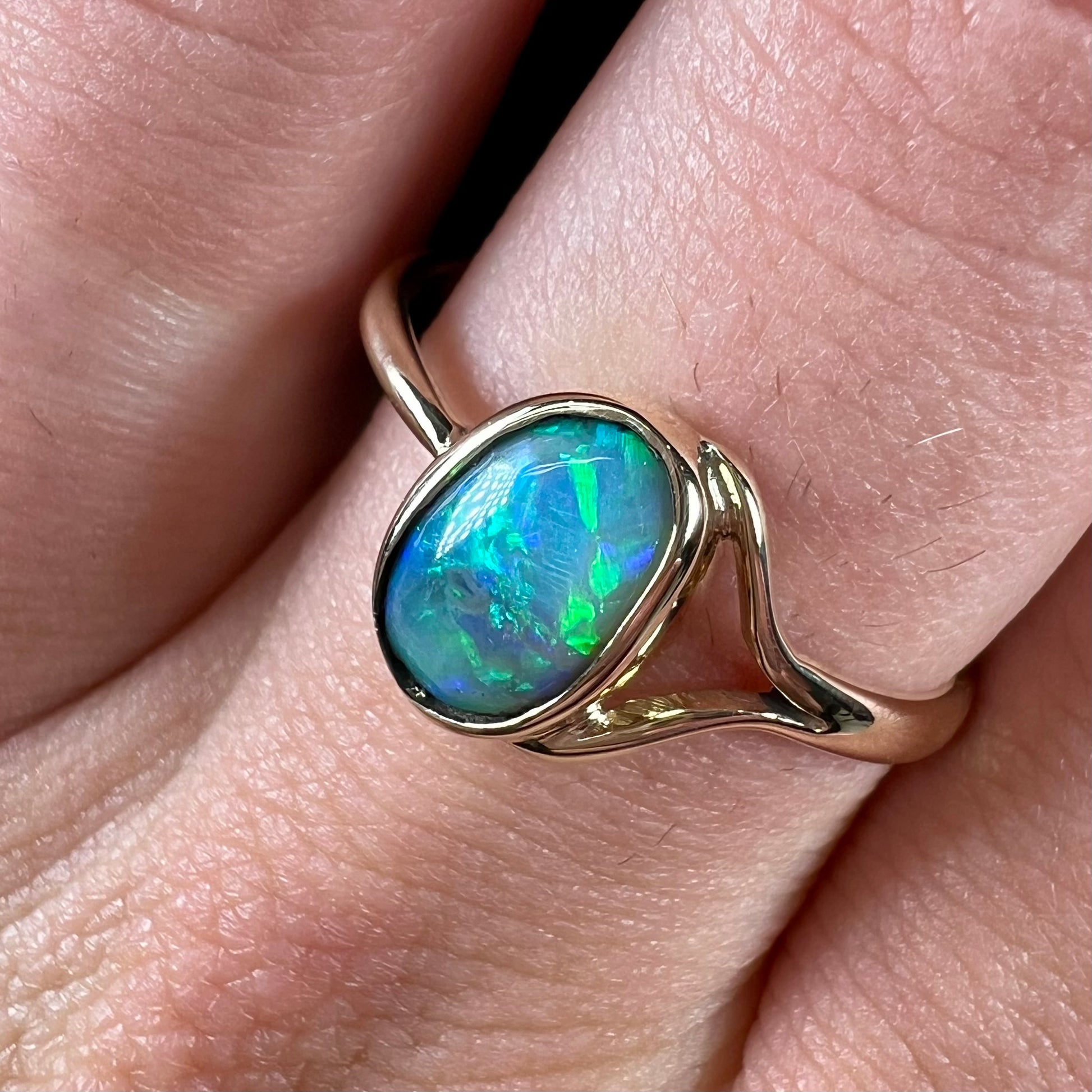 A ladies' oval cut black crystal opal solitaire ring handmade with a single split shank in yellow gold.