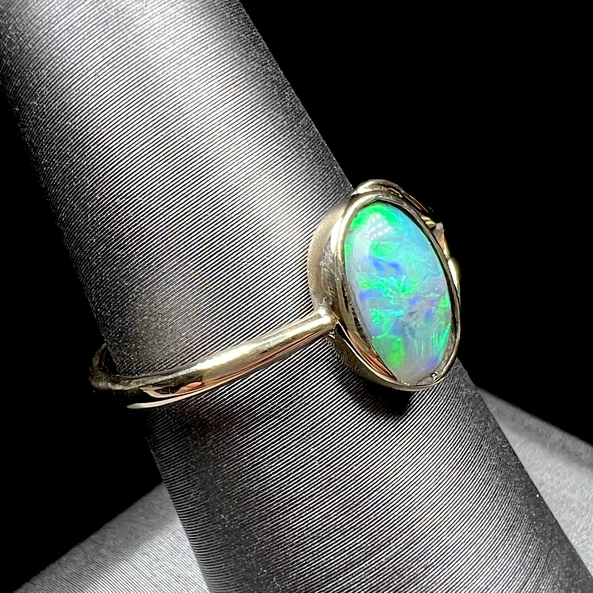 A ladies' oval cut black crystal opal solitaire ring handmade with a single split shank in yellow gold.