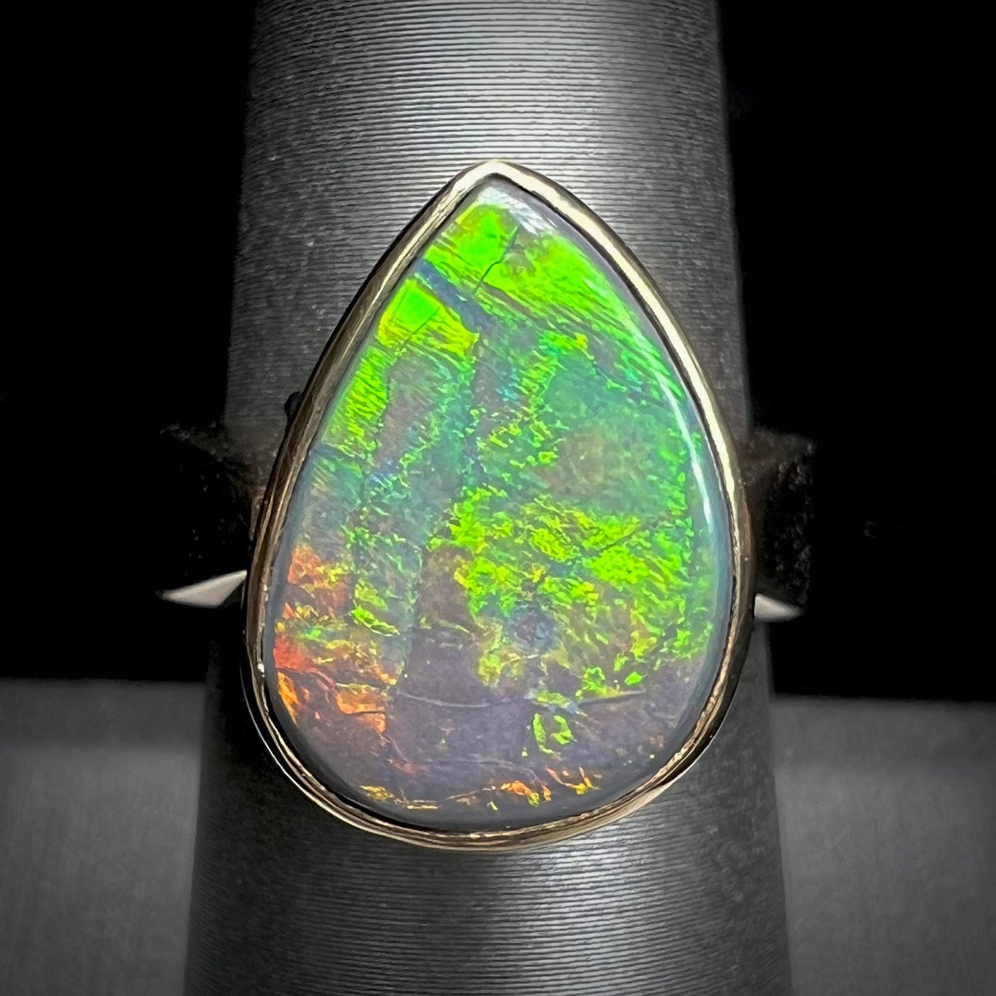 A large ladies' yellow gold solitaire ring set with a natural, pear shaped black crystal opal.  The opal has green and orange fire.