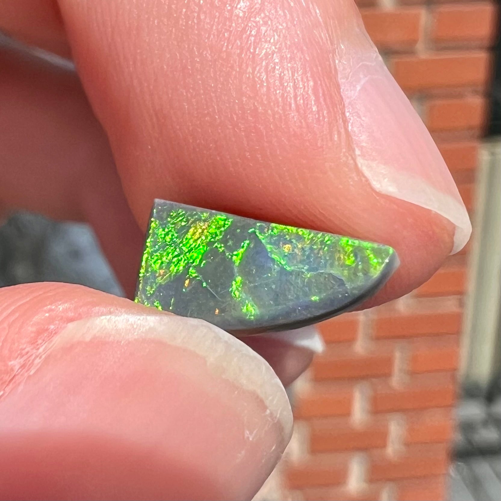 A loose, triangular shaped black opal stone from Lightning Ridge, Australia.  The opal has a bright green flash of color.