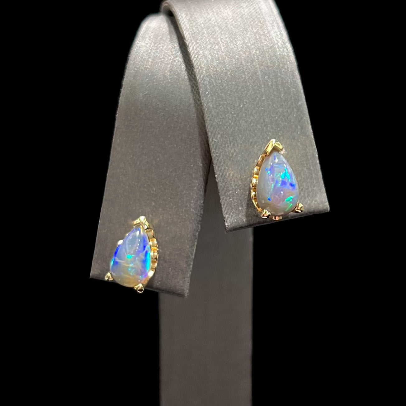 A pair of pear shaped natural black opal stud earrings in filigree style yellow gold baskets.