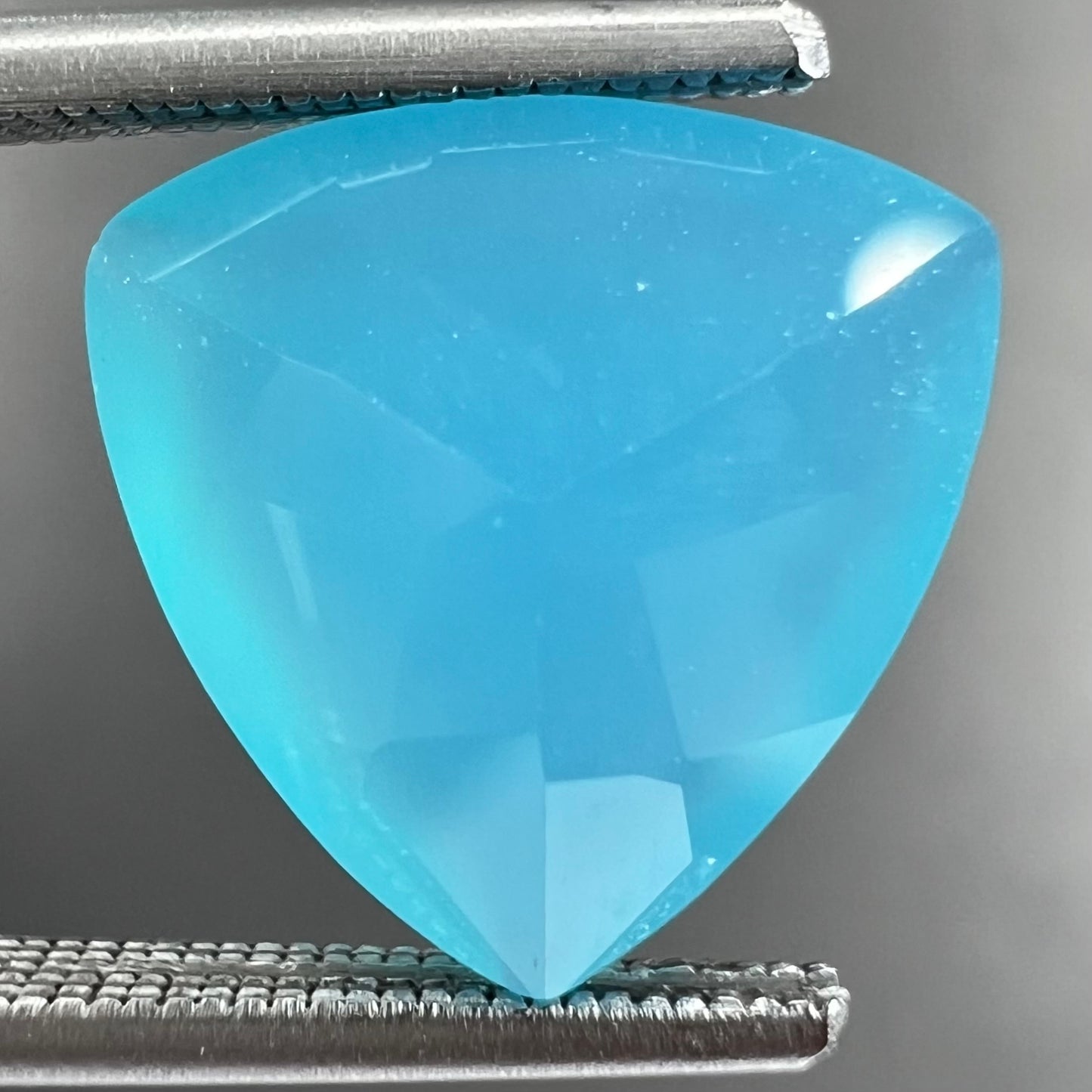 A loose, blue, trillion cut Paraiba chalcedony gemstone.