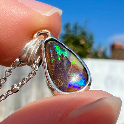 A pear shaped boulder opal necklace in sterling silver.  The opal has bright green and blue flashes.