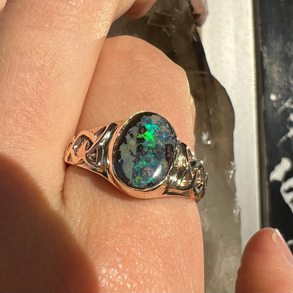 A unisex Celtic style natural boulder opal ring cast in yellow gold.  The opal shines green and blue.