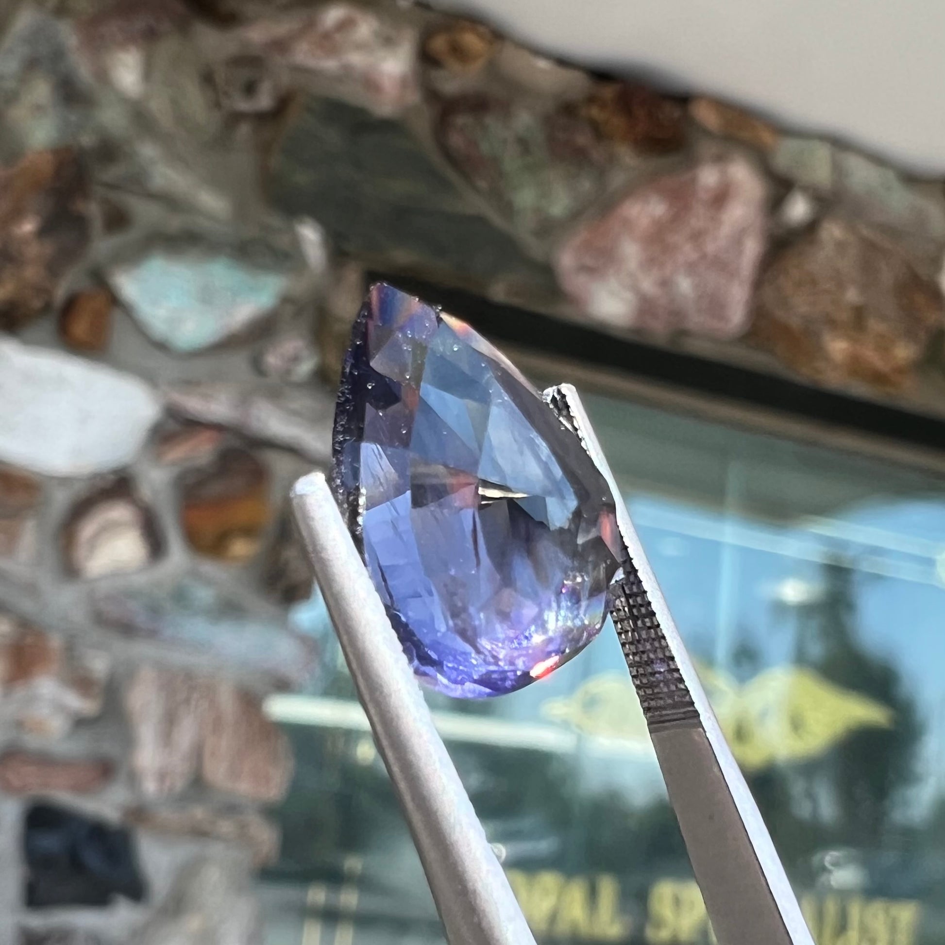 A loose, pear shaped bicolor iolite gemstone.  The stone shows violite purple and silver colors.