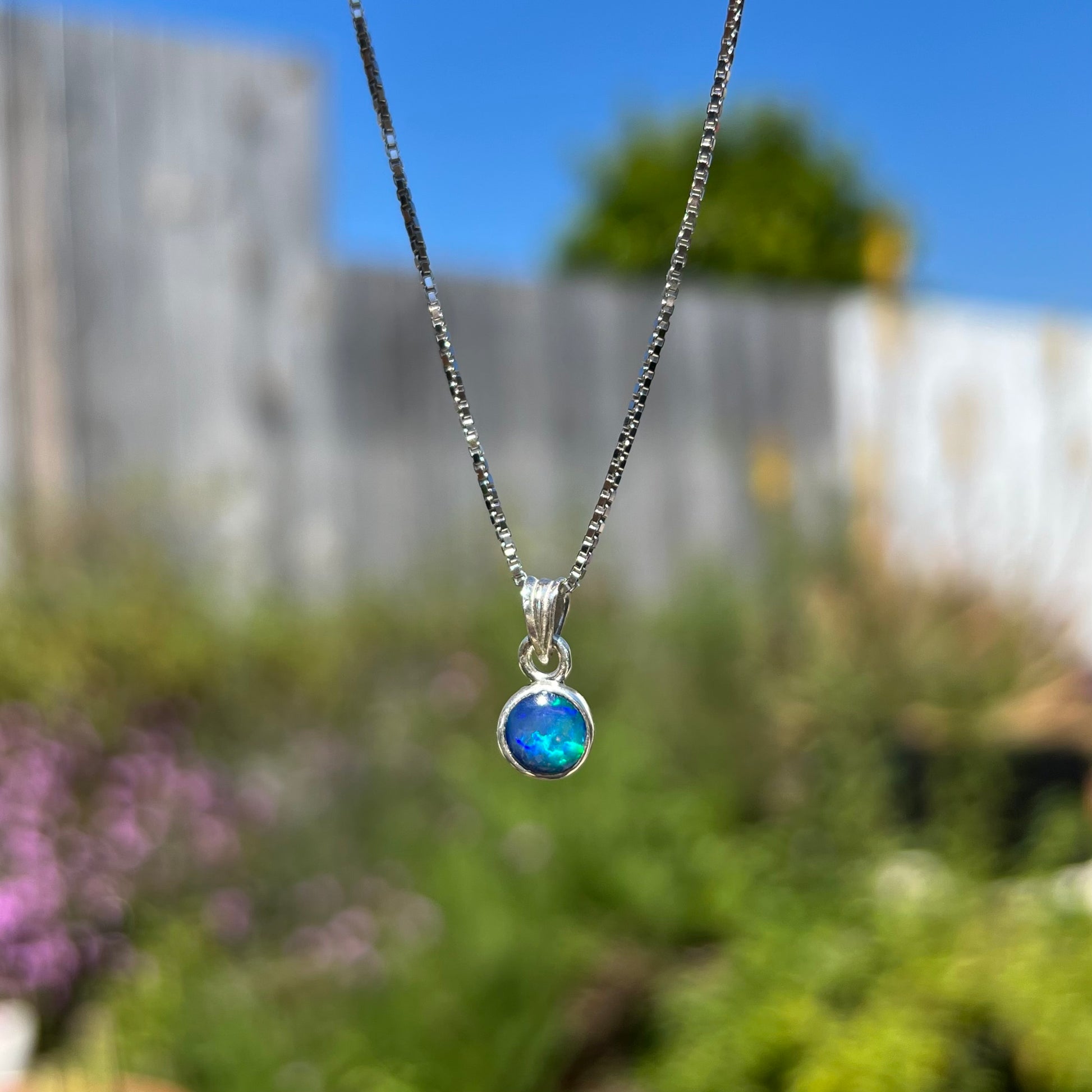 A sterling silver, round cabochon cut black opal solitaire necklace.  The opal has green and blue fire.