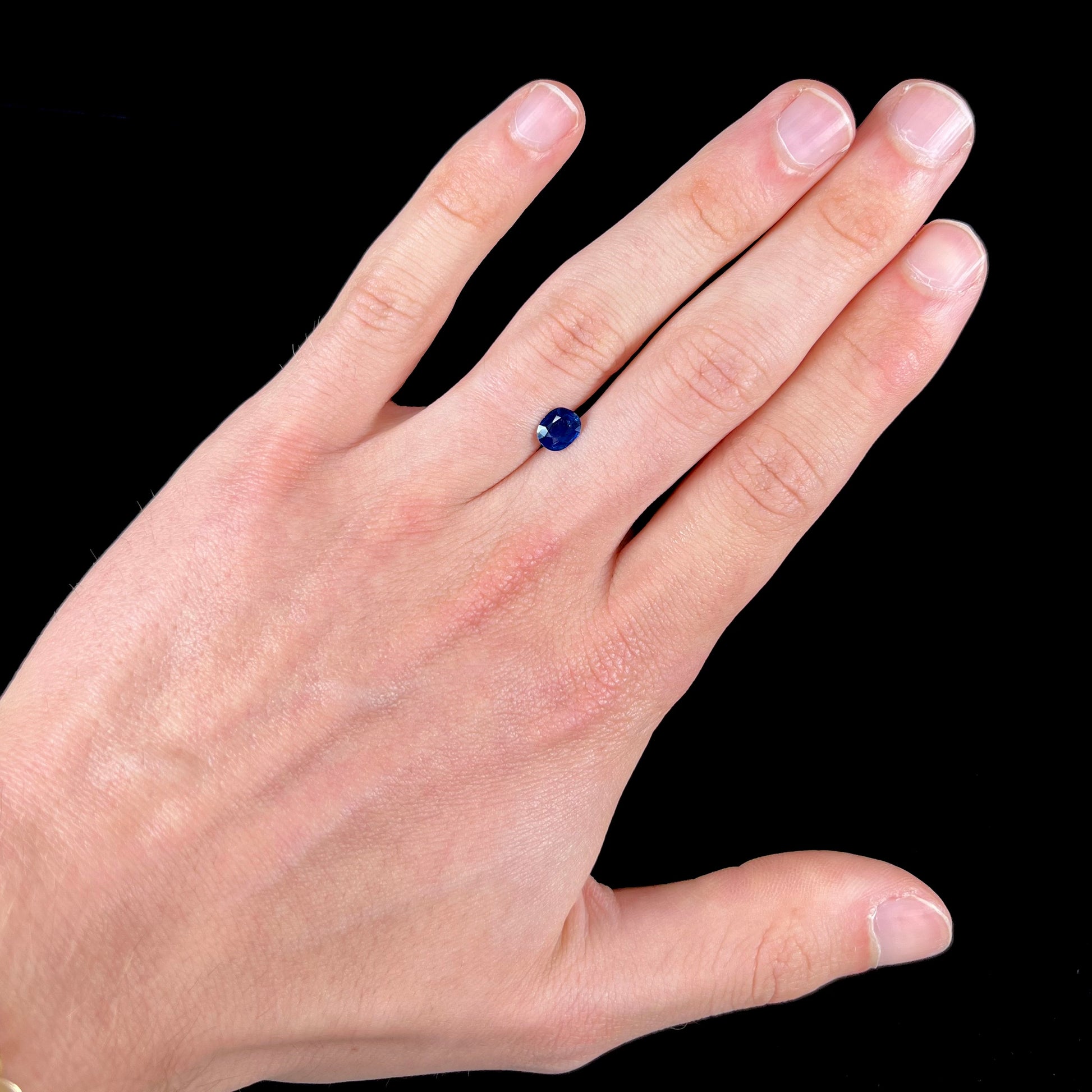 A loose, faceted oval cut dark blue natural sapphire stone.