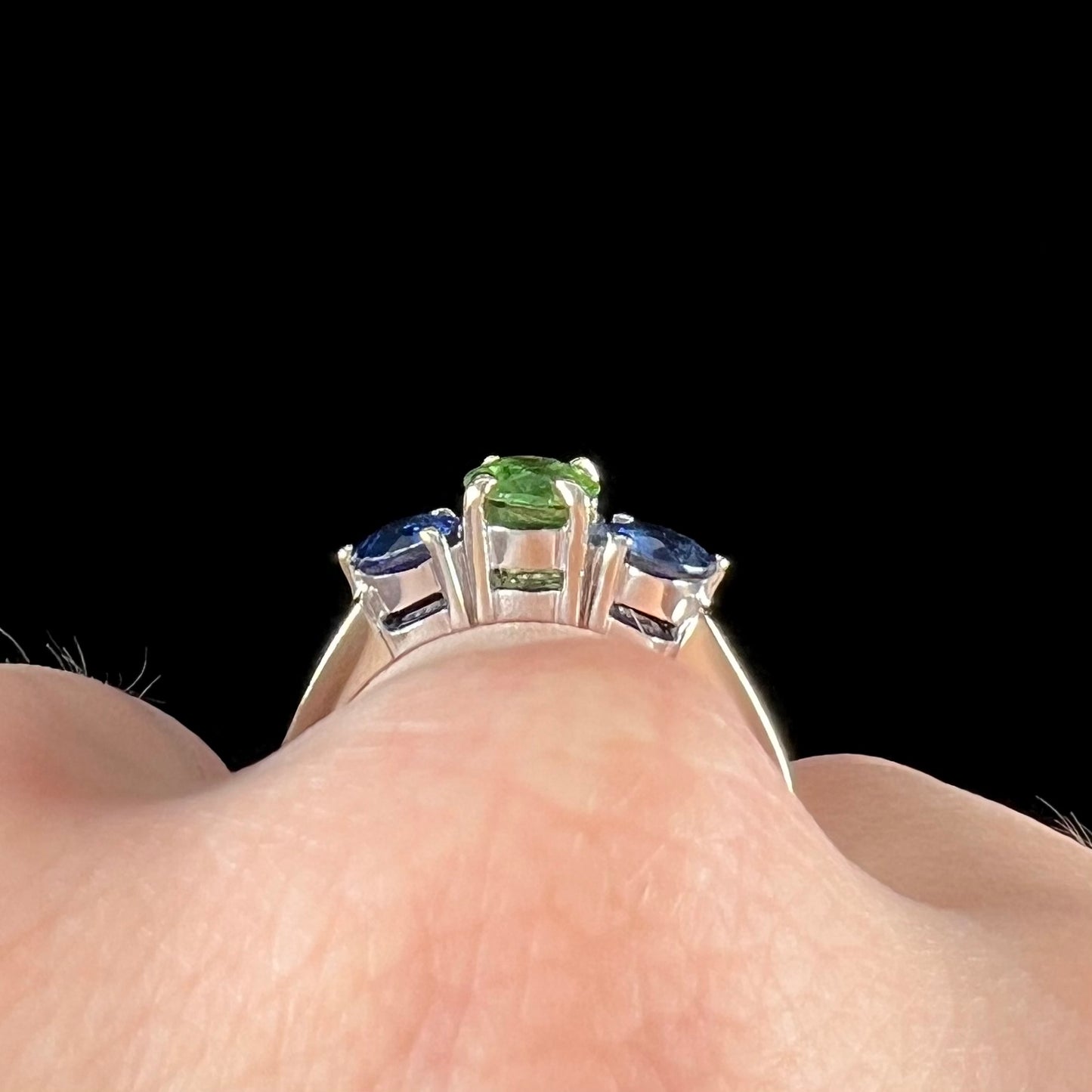 A ladies' white gold three stone ring set with two round blue sapphires and an oval cut green tsavorite garnet.