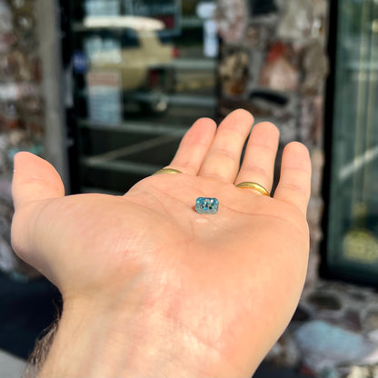 A loose, modified emerald cut blue zircon gemstone.  The stone has a large belly.