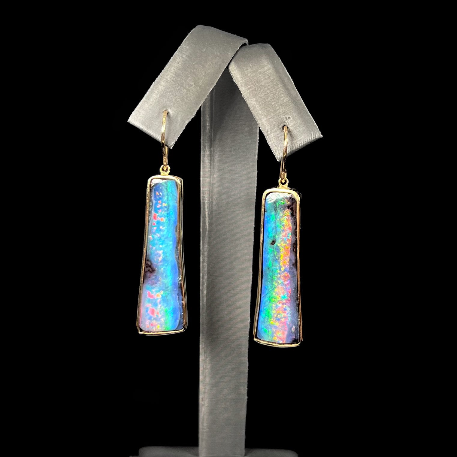 A pair of natural boulder opal dangle earrings set in yellow gold.  The opal displays a rainbow of colors and is from Bull Creek, Australia.