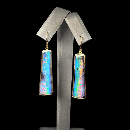 A pair of natural boulder opal dangle earrings set in yellow gold.  The opal displays a rainbow of colors and is from Bull Creek, Australia.