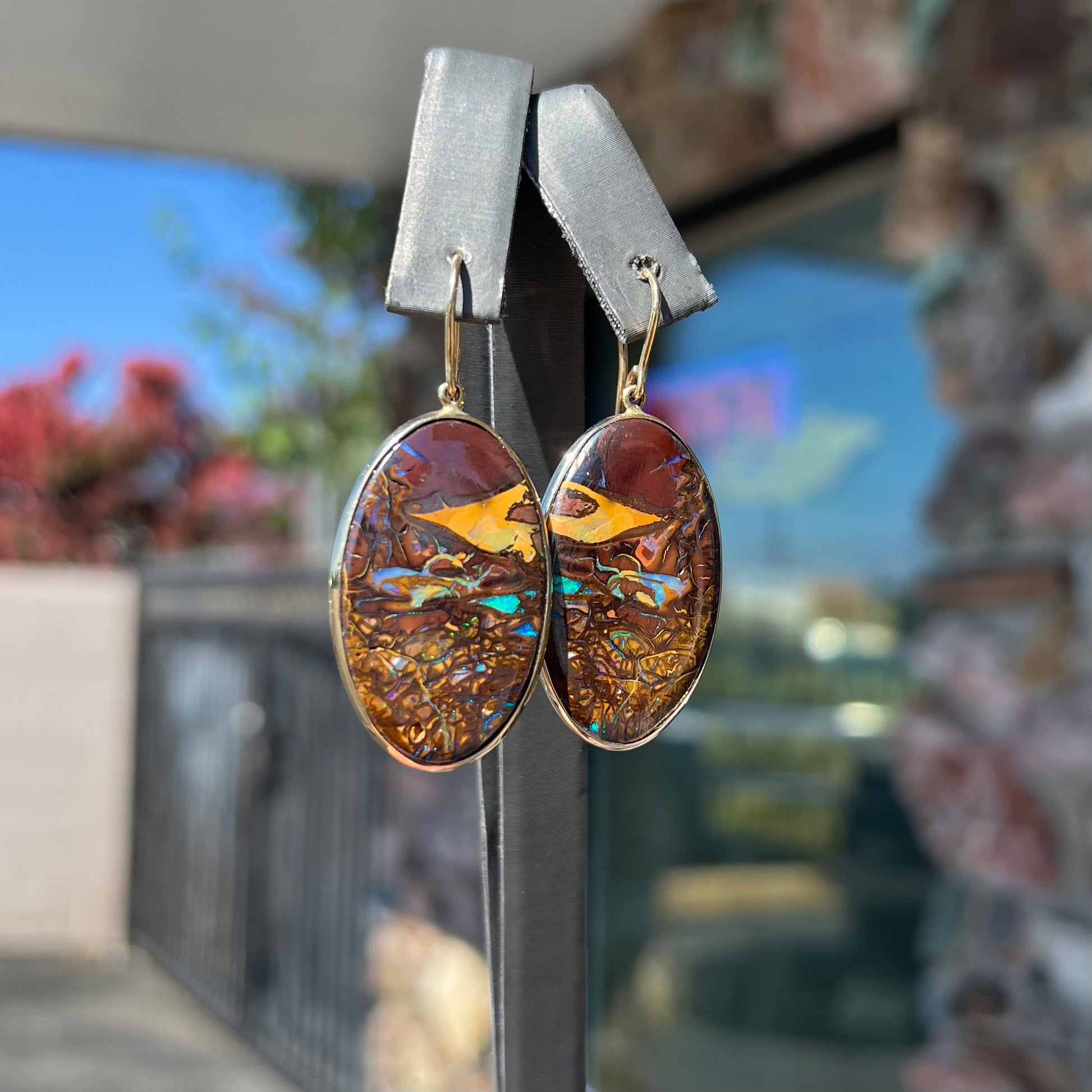 A pair of oval cut Koroit boulder opal dangle earrings in yellow gold bezel frames.  The opal exhibits a unique pattern and blue colors.