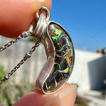 A sterling silver necklace set with a natural Koroit boulder opal shaped like a crescent moon.