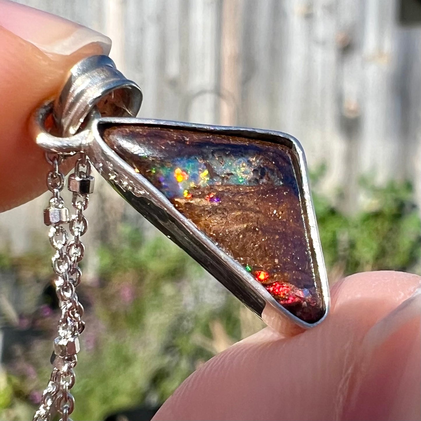 A sterling silver necklace bezel set with a triangle shaped boulder opal.  The opal has red and blue flashes.