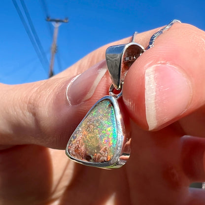 A sterling silver boulder opal necklace on a box chain.  The opal twinkles bright red, green, and blue colors.