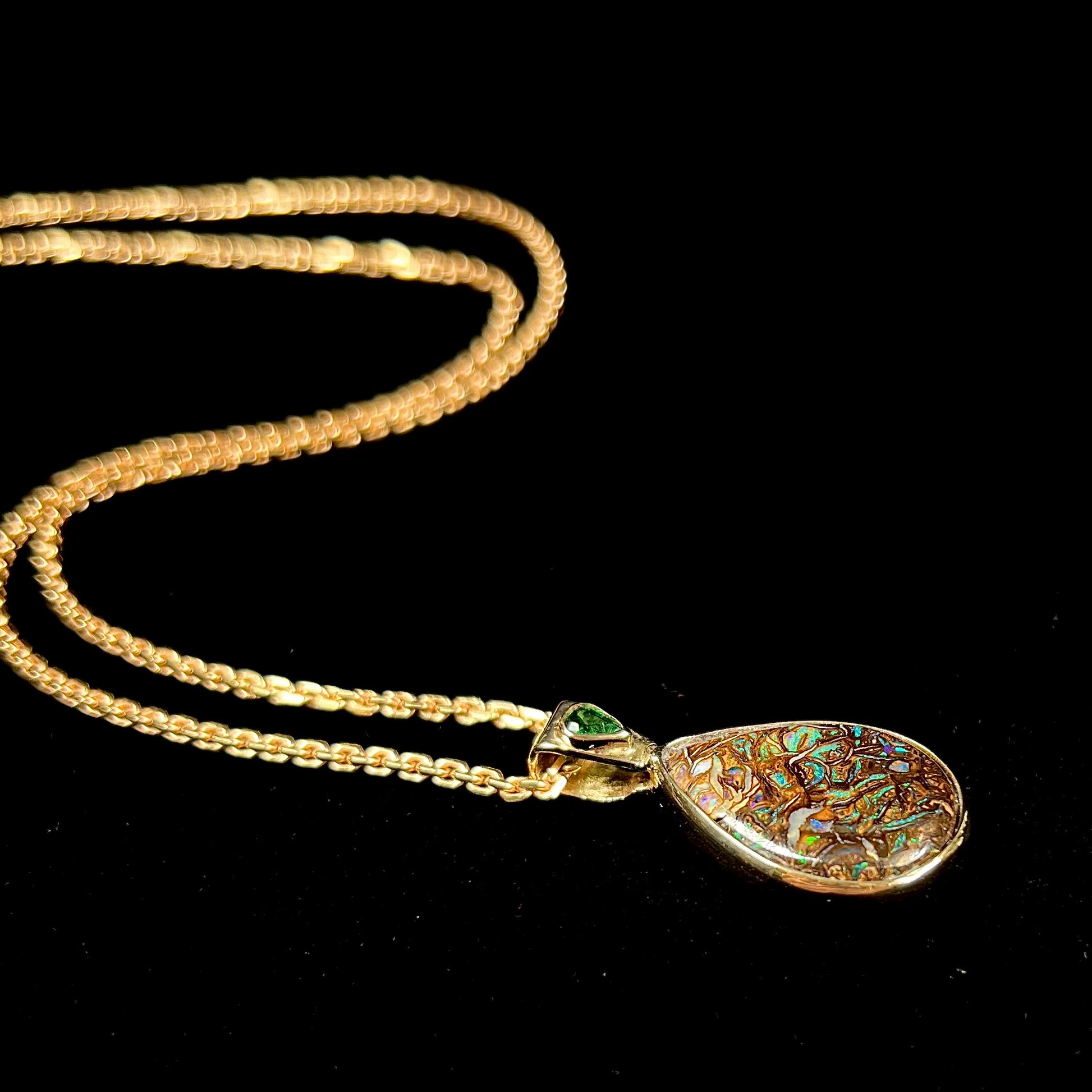 A ladies' yellow gold pendant set with a natural Koroit, Australian boulder opal and a tsavorite garnet accent stone.