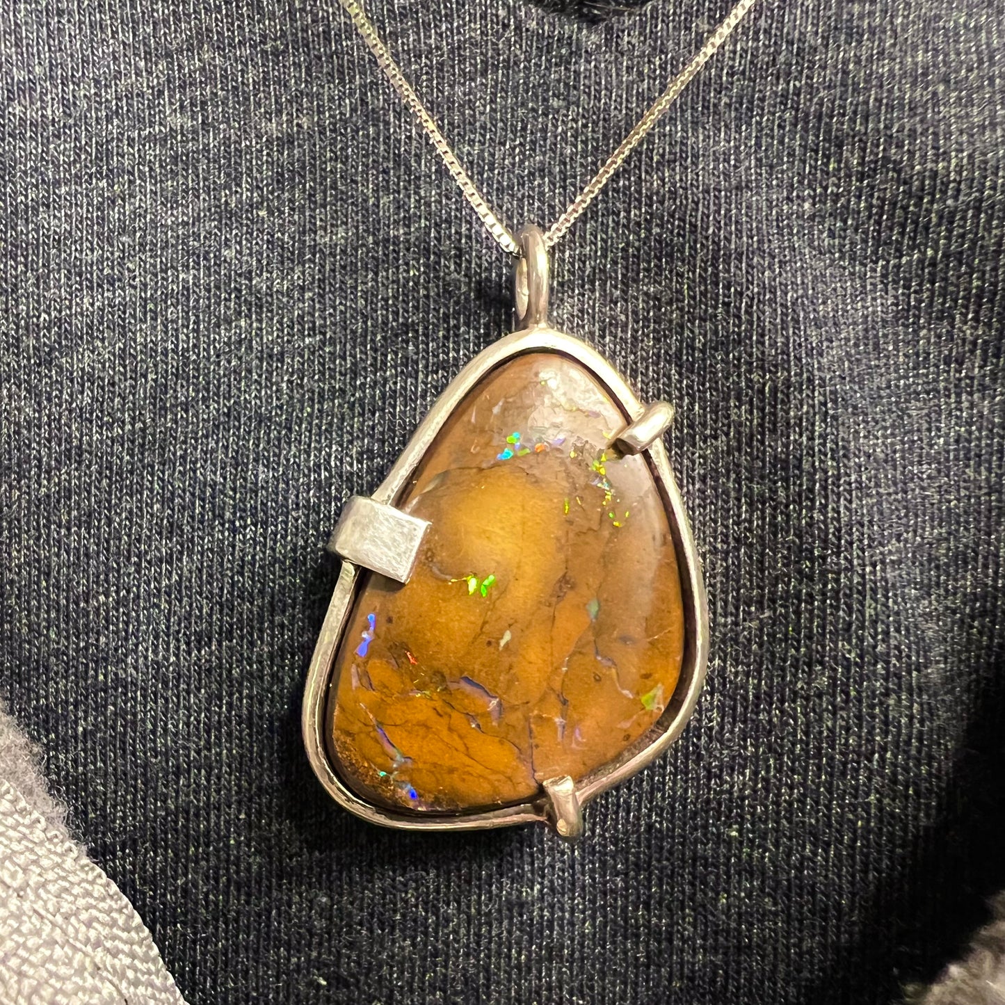 A handmade sterling silver pendant bezel and prong set with a natural boulder opal stone.  The opal shines veins of color.