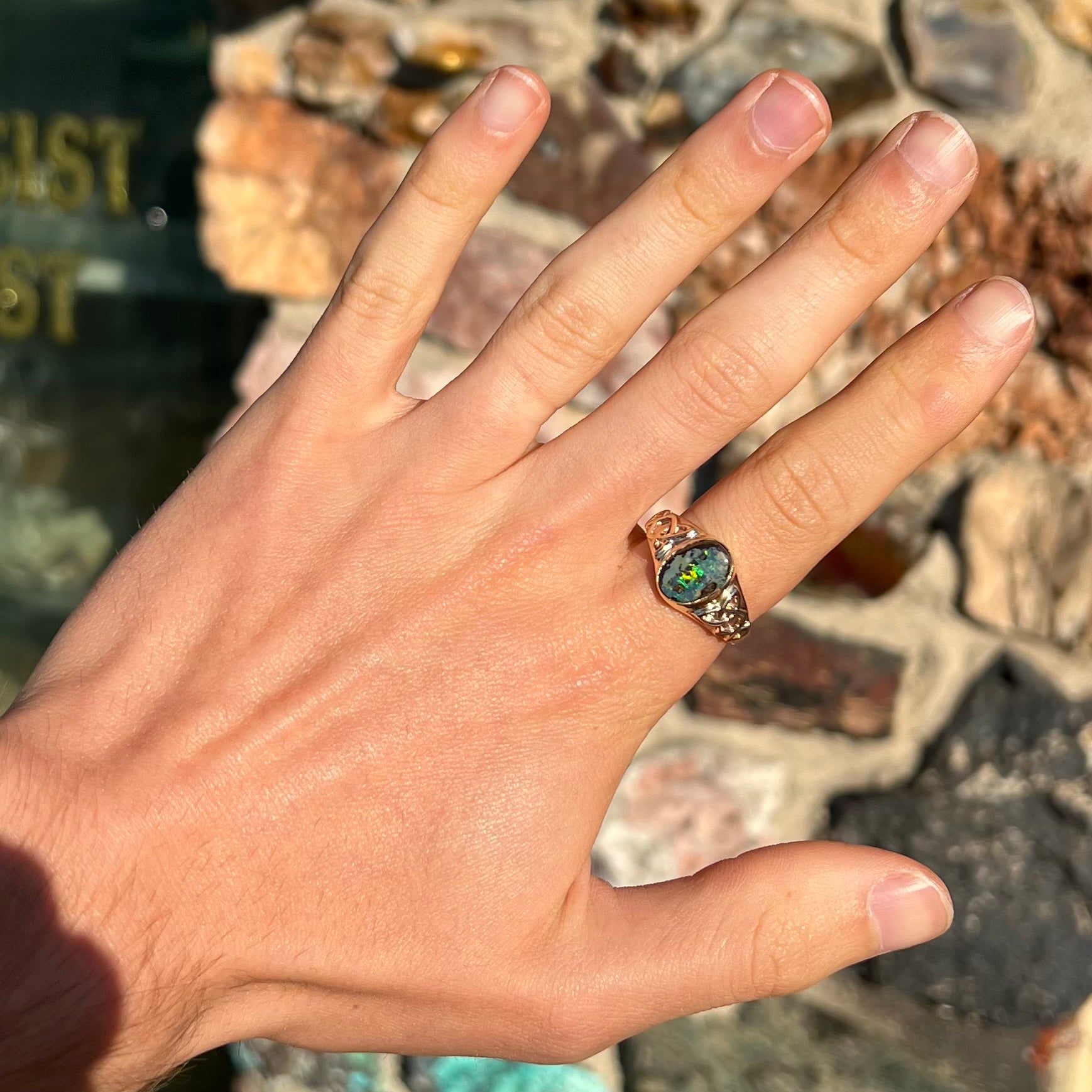 A unisex Celtic style natural boulder opal ring cast in yellow gold.  The opal shines green and blue.