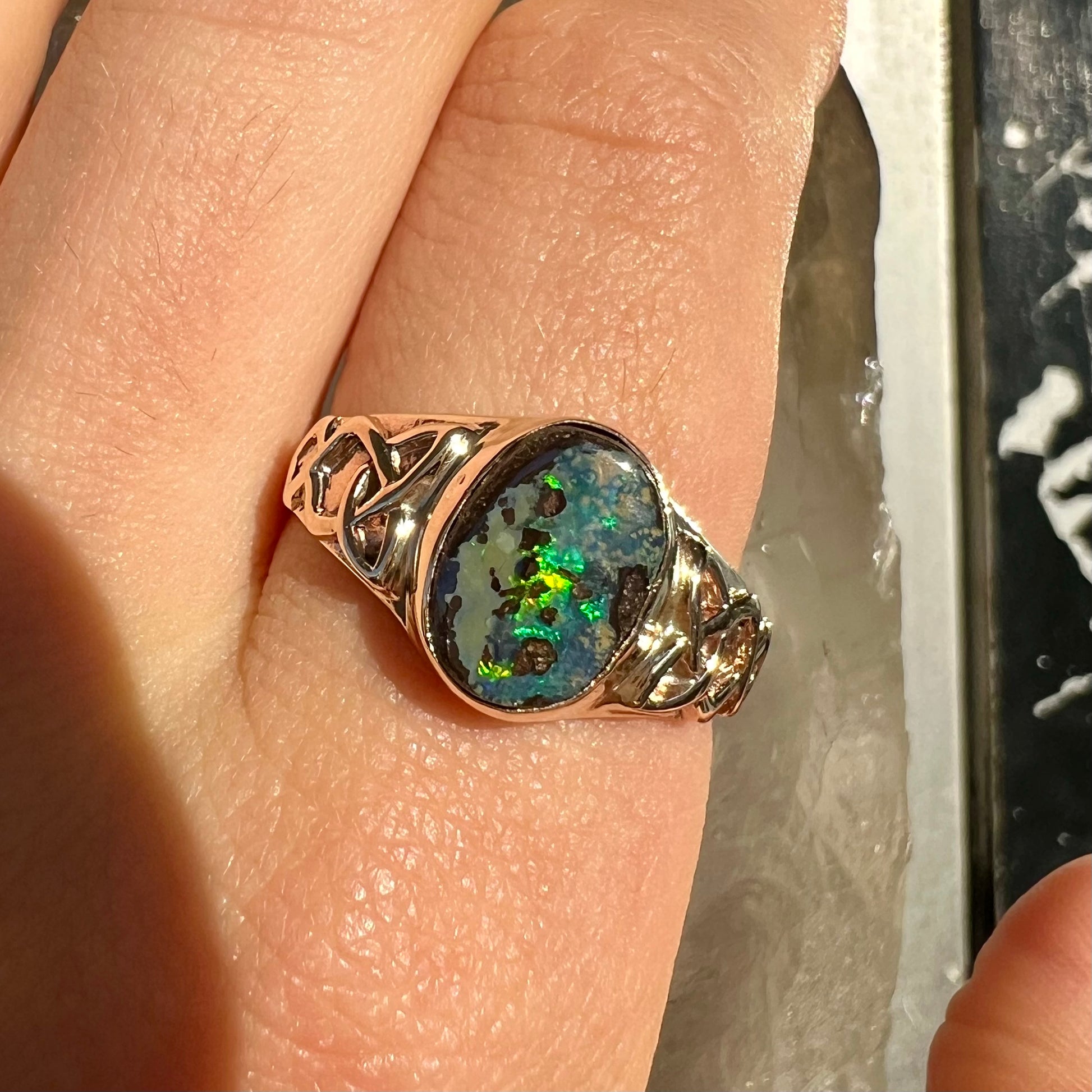 A unisex Celtic style natural boulder opal ring cast in yellow gold.  The opal shines green and blue.