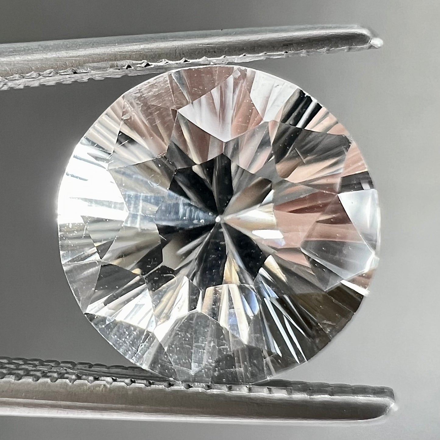 A round brilliant cut petalite gemstone.  The stone is colorless.