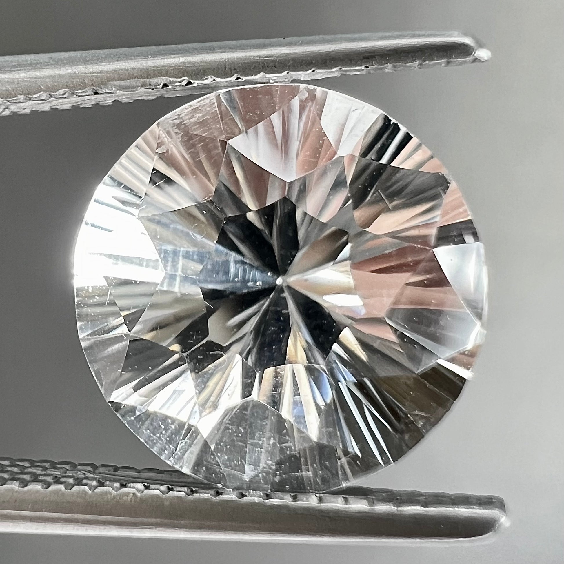 A round brilliant cut petalite gemstone.  The stone is colorless.