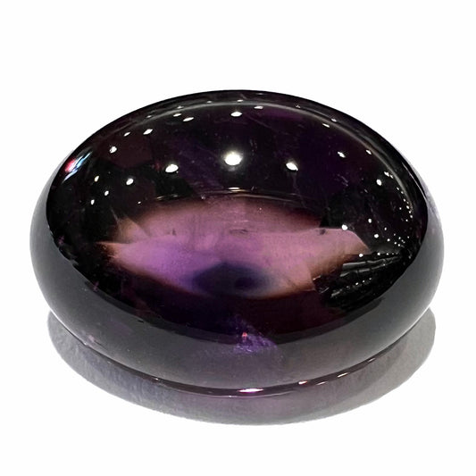 A loose, oval buff top cut amethyst gemstone.  The top of the stone is domed, and the bottom is faceted.  The amethyst weighs 13.14 carats.