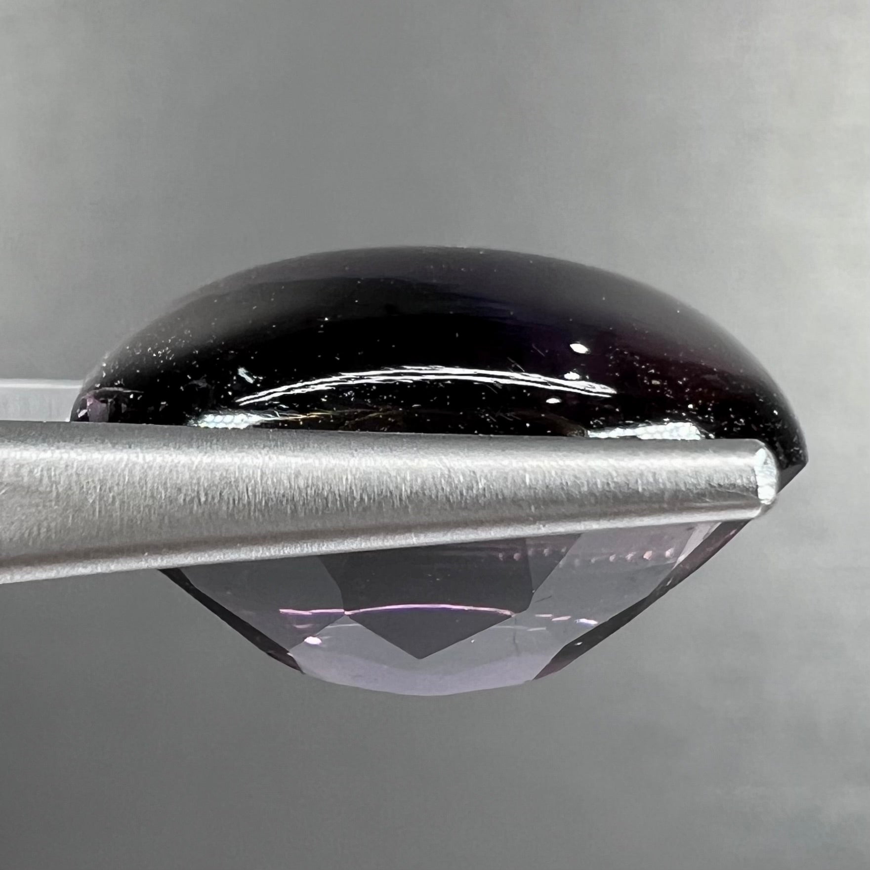 A loose, oval buff top cut amethyst gemstone.  The top of the stone is domed, and the bottom is faceted.