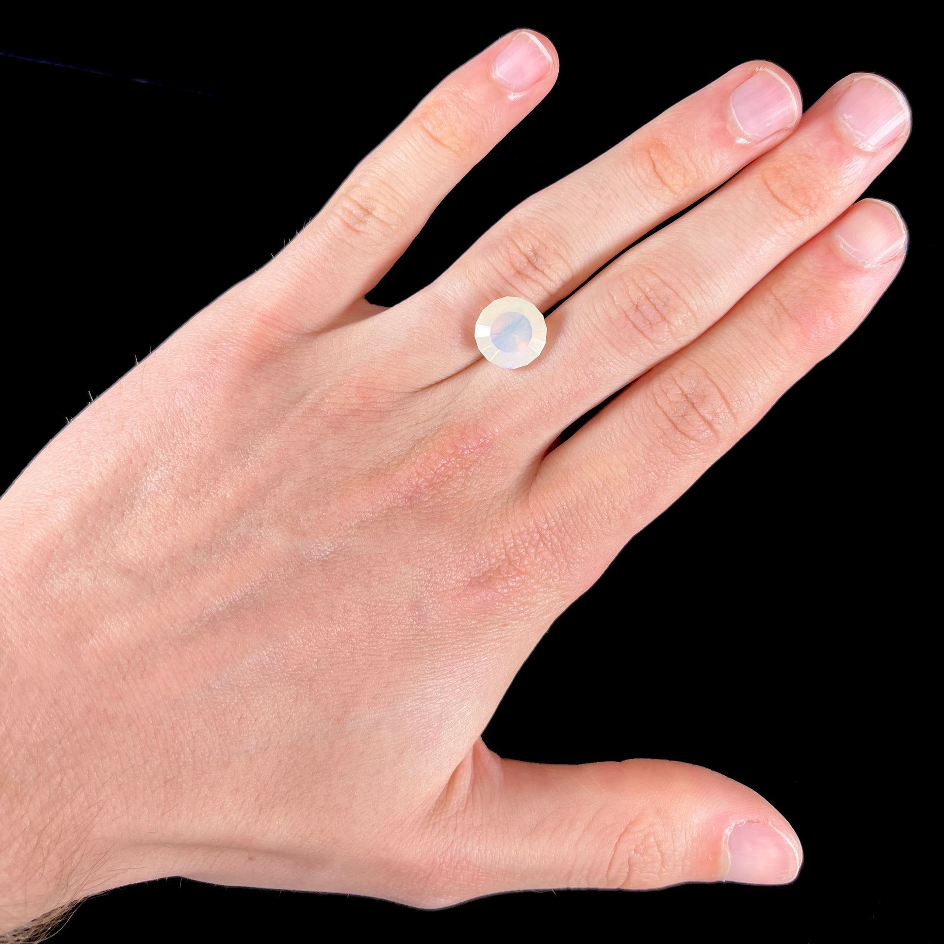 A loose, modified round cut Mexican fire opal gemstone.  The stone is transluscent light yellow with green and blue fire.