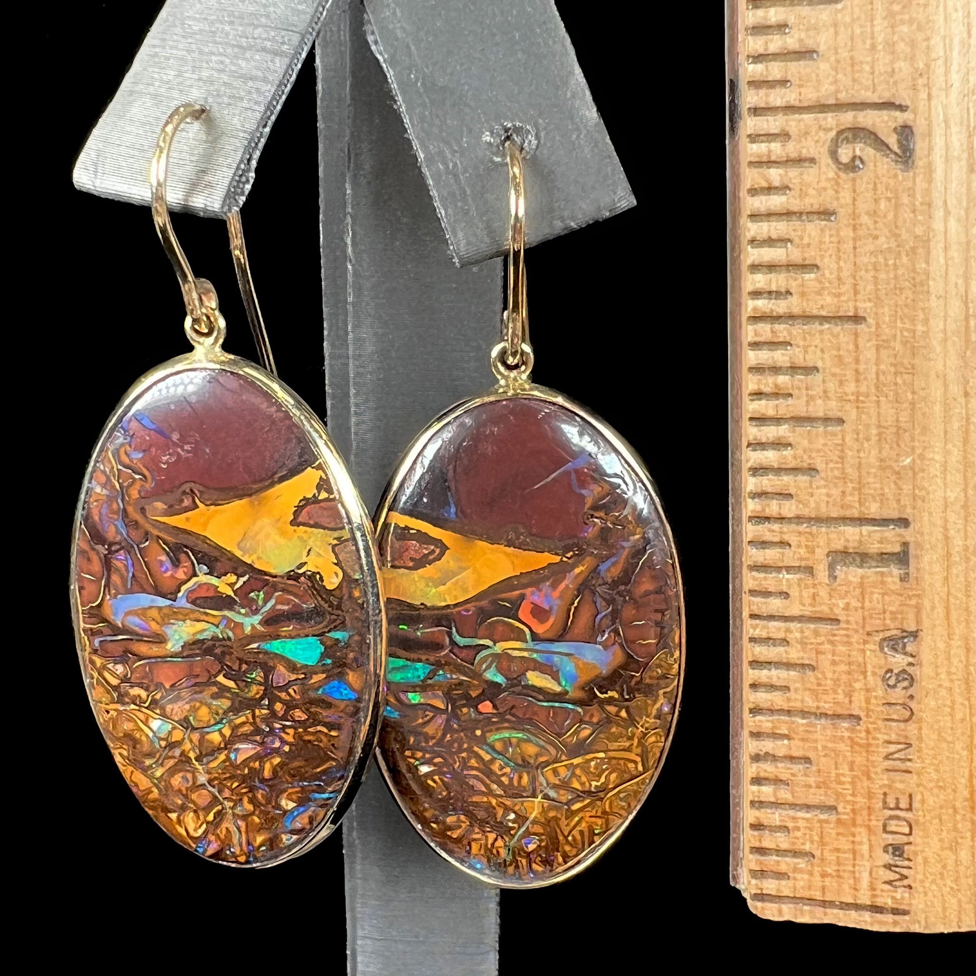 A pair of oval cut Koroit boulder opal dangle earrings in yellow gold bezel frames.  The opal exhibits a unique pattern and blue colors.