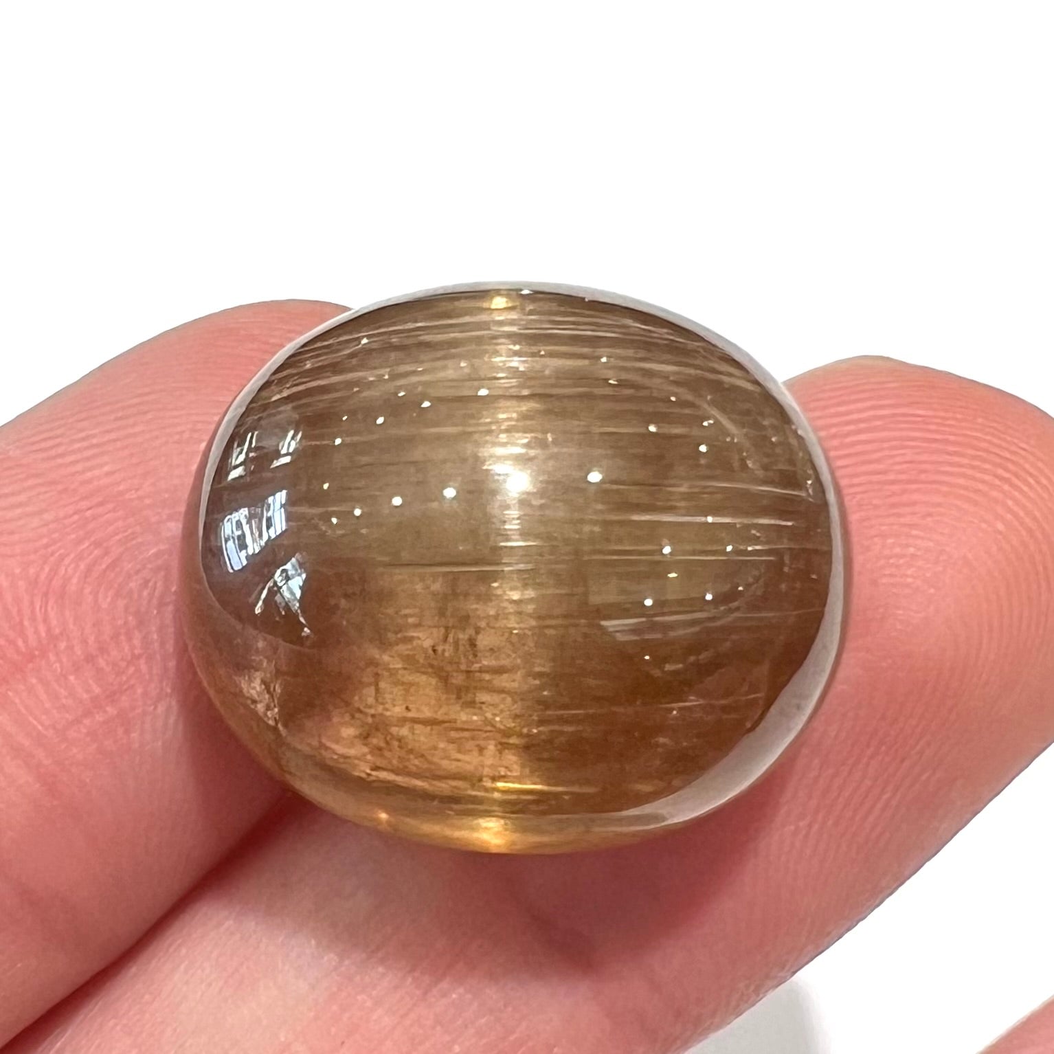 A loose, golden brown cat's eye dravite tourmaline gemstone.  The stone is cut into an oval shaped cabochon.